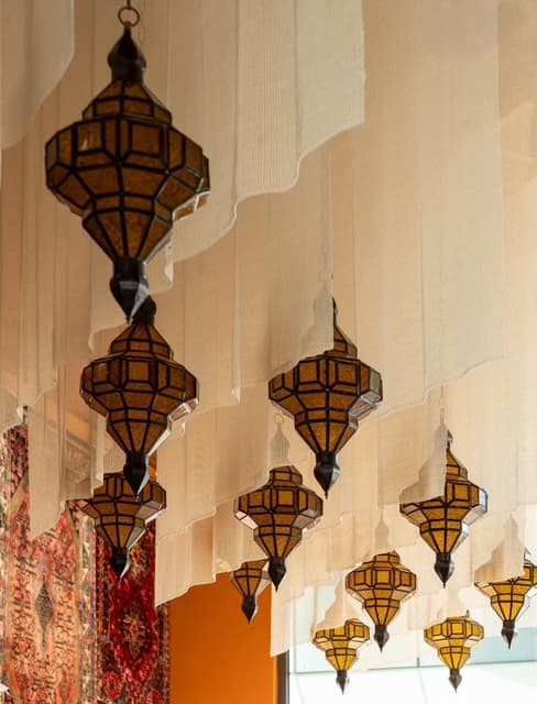 Lanternes orientales en verre ambré suspendues devant des voilages, avec un tapis afghan en arrière-plan