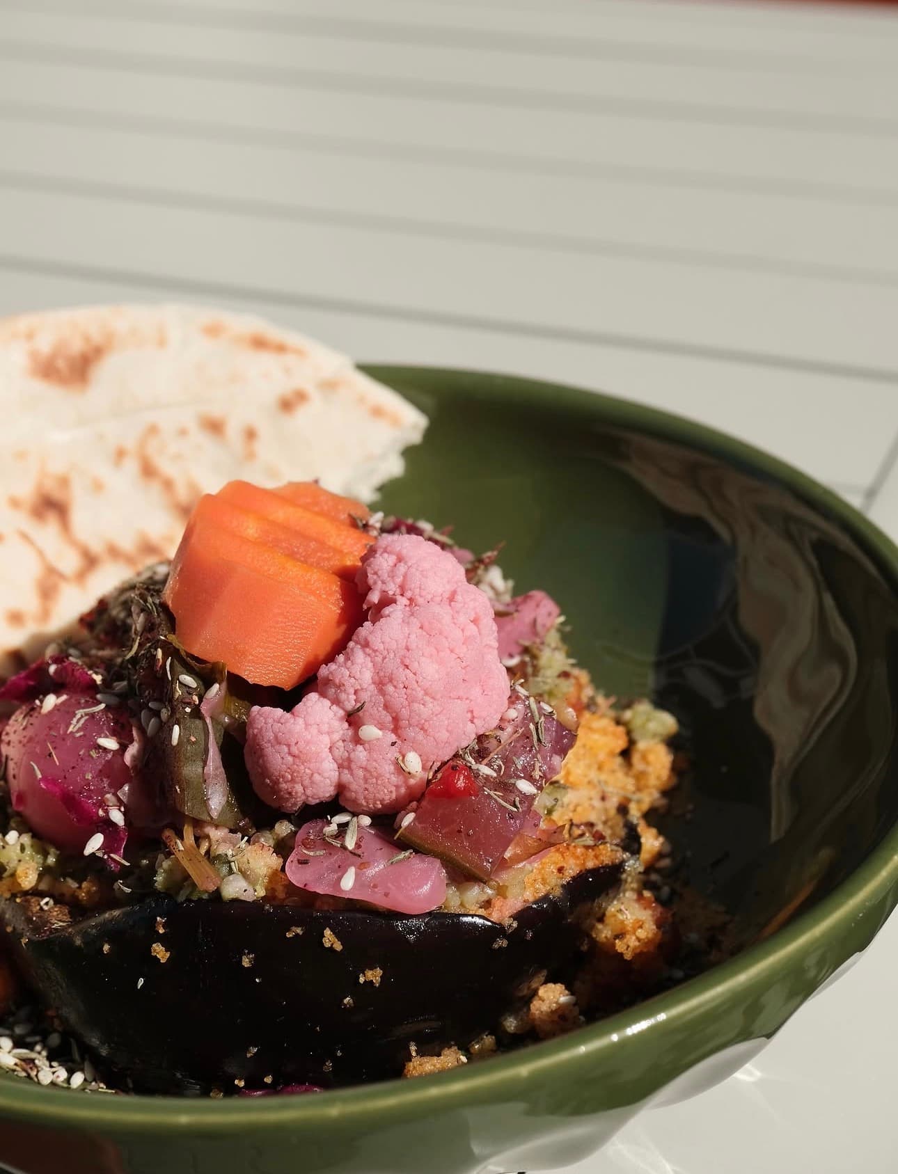 Aubergine, légumes marinés et pain plat dans un bol vert