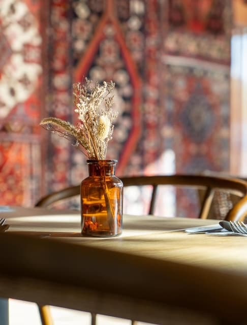 Table dressée avec un bouquet de fleurs séchées devant un mur de tapis